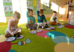 Czwórka dzieci z założonymi rękawiczkami przekłada wykałaczki z jednego talerzyka na drugi.